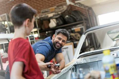Smiling father taking tool from son in auto repair shop Stock Photos