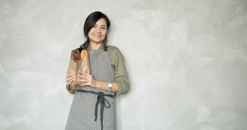 Smiling female baker looking at the camera and giving a bag with baguettes Stock Footage 134592028