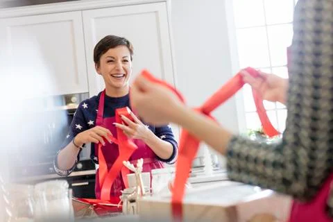 Smiling female caterers wrapping baked goods in boxes with red ribbon in kitchen Stock Photos