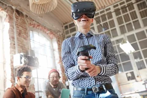 Smiling female computer programmer testing virtual reality simulator glasses and Stock Photos