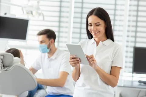 Smiling female dentist using digital tablet while her collegue working with s Stock Photos