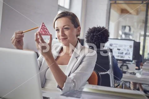 Smiling female design professional examining triangle prototype at laptop in Stock Photos