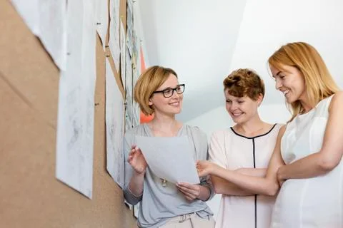 Smiling female designers reviewing proofs at bulletin board in office Stock Photos