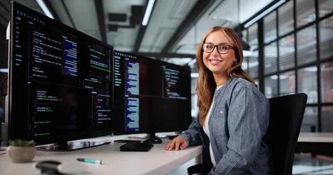 Smiling Female Developer Coding On Numerous Monitors In Computer Office. Stock Photos