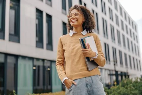 Smiling female freelancer standing with laptop and note pads on modern building Stock Photos