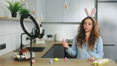 Smiling female influencer talking of Easter eggs coloring for video blog at home Stock Footage 231344326