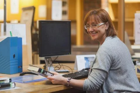Smiling female librarian holding a book standing behind the desk Stock Photos