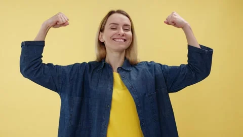 Smiling female looking at biceps while standing in studio with yellow background Video stock 265934883