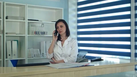 Smiling female nurse answering phone call at the reception desk Stock Footage