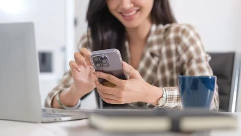 Smiling female office worker using smartphone, chatting over the internet o.. Stock-Fotos
