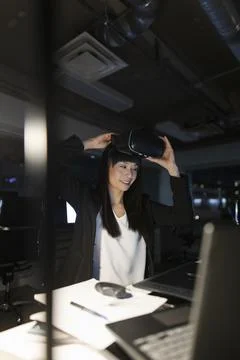 Smiling female programmer with VR headset working late in office Stock-Fotos
