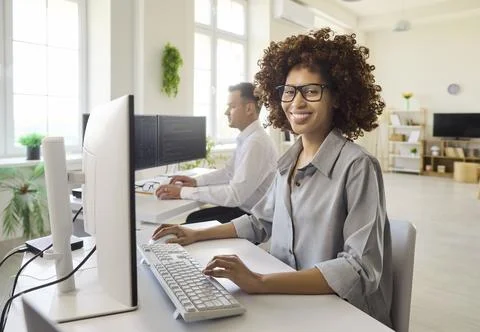 Smiling female software developer coding at desktop in bright modern office Stock Photos