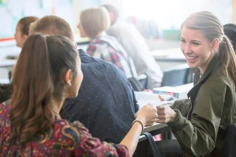 Smiling female students exchanging notes in classroom Stock Photos