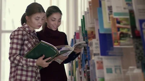 Smiling female students in library reading something funny in a book Stock-Footage 73313680