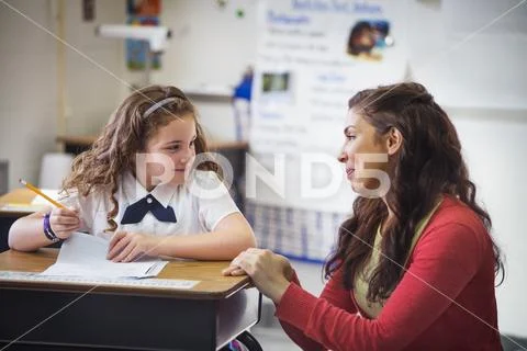 Smiling female teacher looking at schoolgirl in classroom Stock Photos