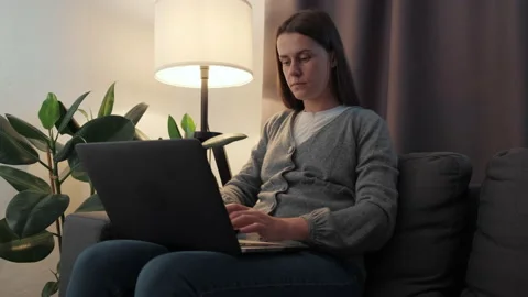 Smiling female using laptop notebook sit on couch under night lamp at home Video stock 202123513