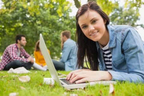 Smiling female using laptop with other students in park Foto stock