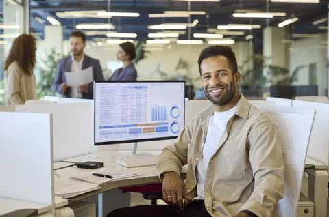 Smiling financial analyst at desk with data dashboard and charts in office 写真素材
