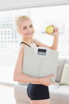 Smiling fit woman in sportswear holding scale and apple Stock Photos