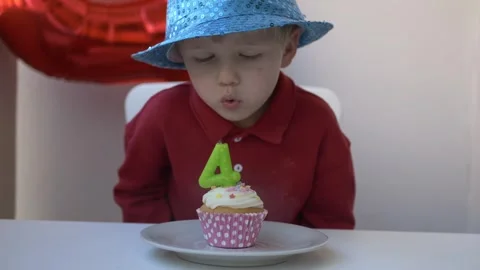 Smiling four-year-old boy in blue hat makes a wish and blows out the number four Stock Footage 316084469