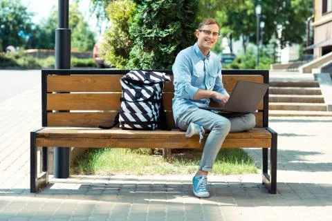 Smiling freelancer feeling busy while finishing work sitting on the bench Stock Photos