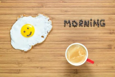 Smiling fried egg lying on a white plate and wooden cutting board with silver Stock Photos