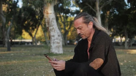 Smiling friendly mature freelancer holding smartphone sitting in park. Stock Footage 223364828