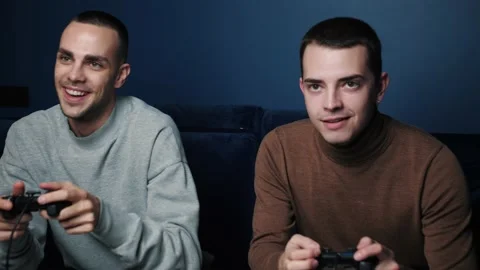 Smiling friends with gamepads joystick controller playing video game on sofa at Stock Footage 144492926