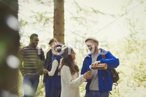 Smiling friends hiking pouring coffee from insulated drink container in woods Stock Photos