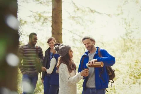 Smiling friends hiking pouring coffee from insulated drink container in woods Stock Photos