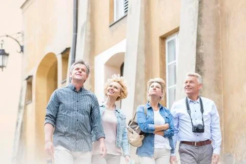 Smiling friends looking up while walking by building Fotos de archivo