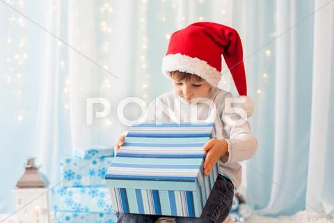 Smiling funny child in Santa red hat holding Christmas gift in hand Stock Photos