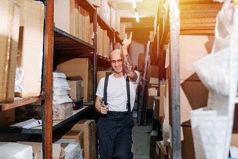 Smiling funny warehouse worker dance-walking between tall rows of shelves Stock Photos