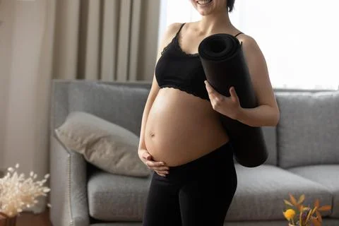 Smiling future mom touching tummy holding rolled up yoga mat Stock Photos