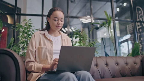 Smiling game developer working on laptop, sitting on sofa in office, education Stock Footage 159822113