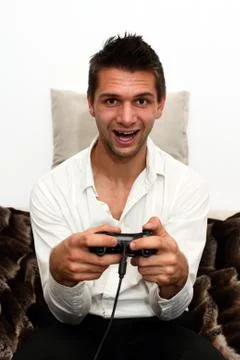 Smiling gamer sitting on couch with controller and playing Stock Photos