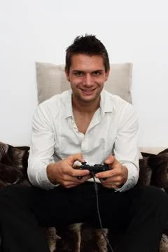Smiling gamer sitting on couch with controller and playing Stock Photos