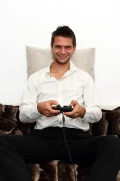 Smiling gamer sitting on couch with controller and playing Foto stock