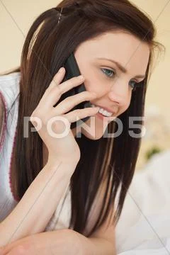 Smiling girl calling someone with a mobile phone lying on a bed Stock Photos