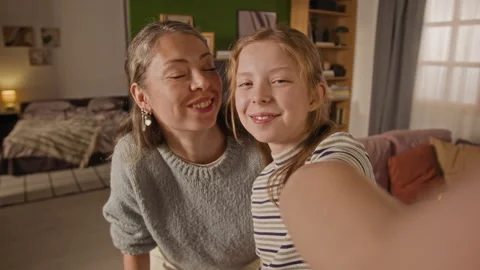 Smiling Girl Child Pulling Faces while Taking Selfie with Mother in Living Room Stock Footage 334331118