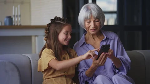Smiling girl explaining how to use a new mobile app to her grandmother, pastime 動画素材 337094052