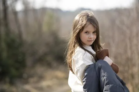 Smiling girl facing camera with jacket in hand outside on path in forest. Con Stock Photos