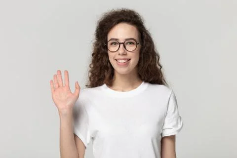 Smiling girl in glasses looking at camera wave hand studioshot Stock Photos