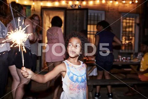 Smiling girl holding burning sparkler at backyard party Stock Photos