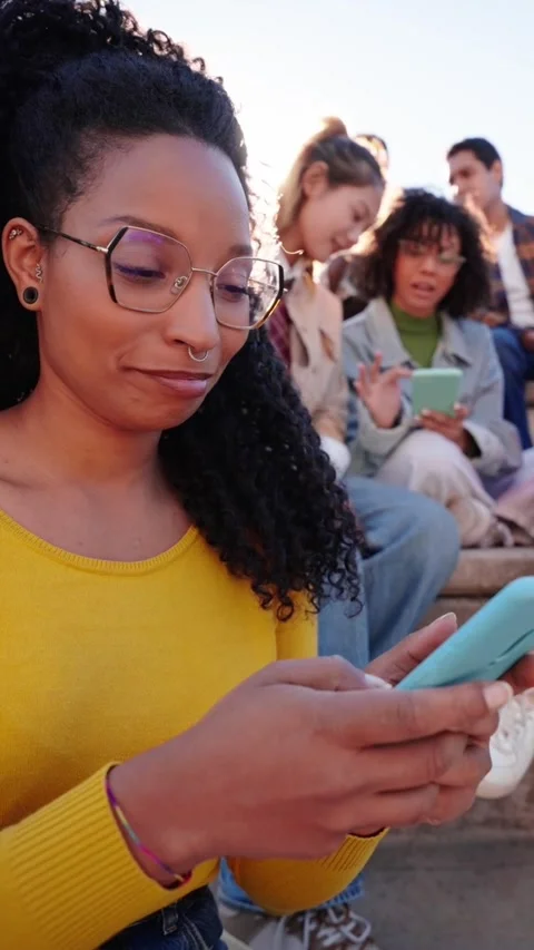 Smiling girl looking at camera using holding her phone sitting on city street Stock Footage 268645310