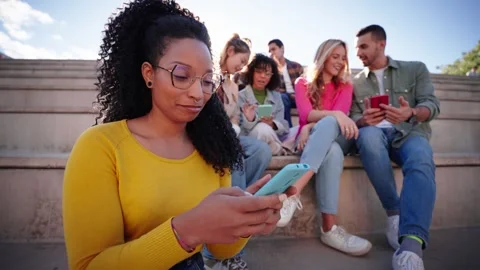 Smiling girl looking at camera using holding her phone sitting on city street Stock Footage 269728515