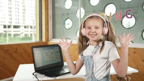 Smiling girl looking at camera while waving hand with laptop placed. Erudition. Stock Photos