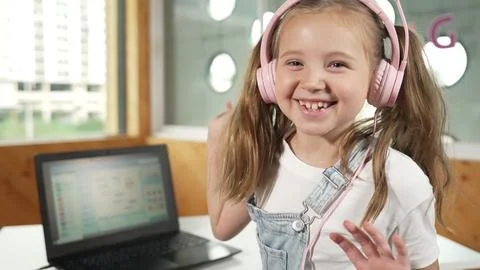 Smiling girl looking at camera while waving hand with laptop placed. Erudition. Stock Photos