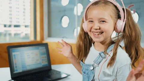 Smiling girl looking at camera while waving hand with laptop placed. Erudition. Stock Photos