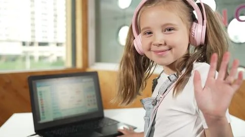 Smiling girl looking at camera while waving hand with laptop placed. Erudition. Stock Photos